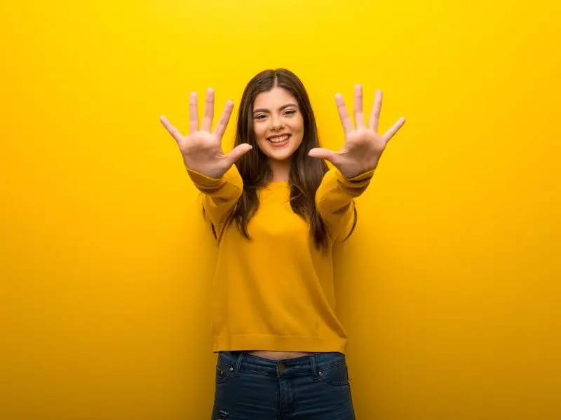 10 of Our Favourite WordPress Plugins picture shows a lady in a bright yellow jumper holding up all 10 fingers - concept for top ten favourite WordPress plugins