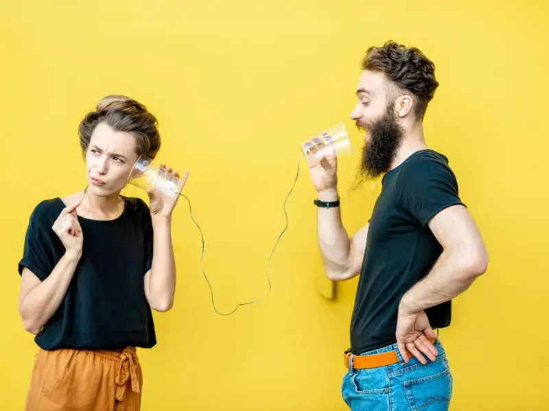 Are You Telling Your Customers What They Want to Hear? This image shows a man communicating with a customer through a string and cups set up, the woman looks confused - concept for marketing communications