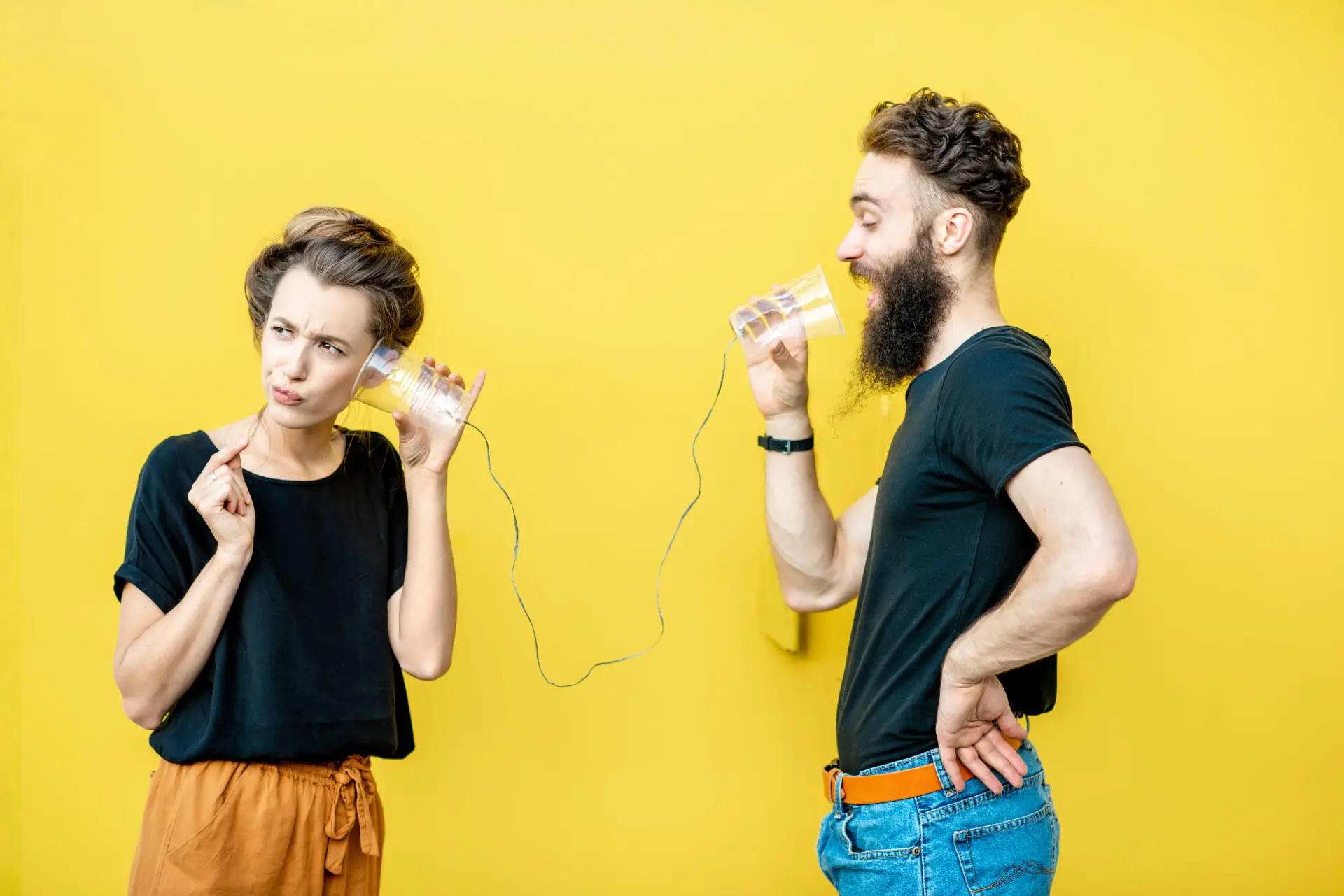 Are You Telling Your Customers What They Want to Hear? This image shows a man communicating with a customer through a string and cups set up, the woman looks confused - concept for marketing communications