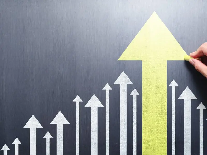 Business Development versus Personal Development this image shows a black board with various ascending arrows a hand is drawing the largest yellow arrow - concept for both business and personal development