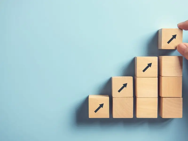 Developing Northamptonshire. The image shows a blur background with square, wooden bloacks laid out in an ascending graph format with upward arrows and a hand placing the top one - business development concept