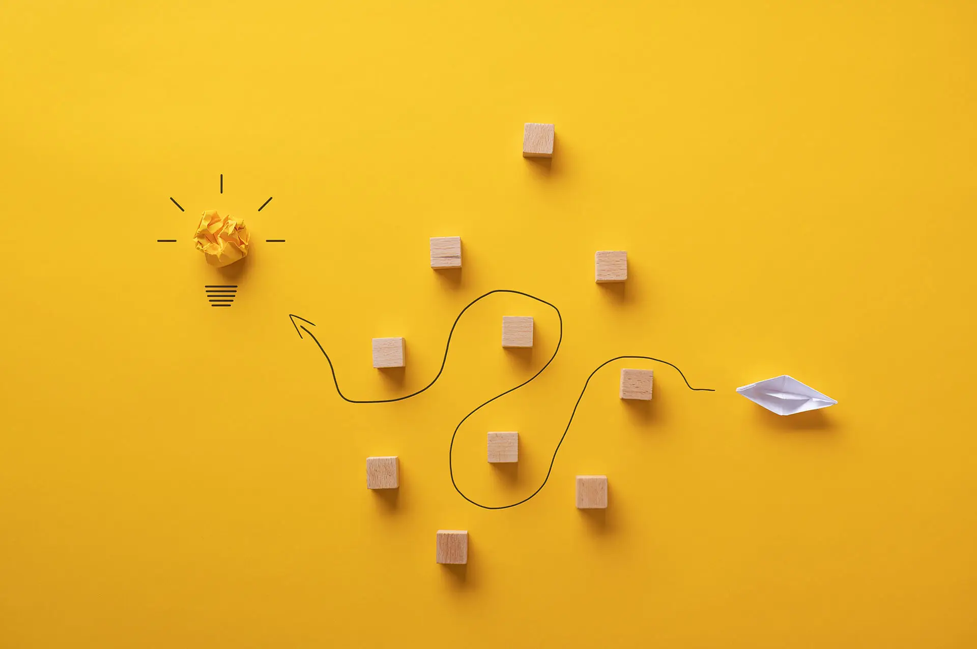 Eight Paths to Effective Networking the image shows a bright yellow background with a paper boat navigating a path around wooden blocks to reach a lightbulb moment - effective networking concept