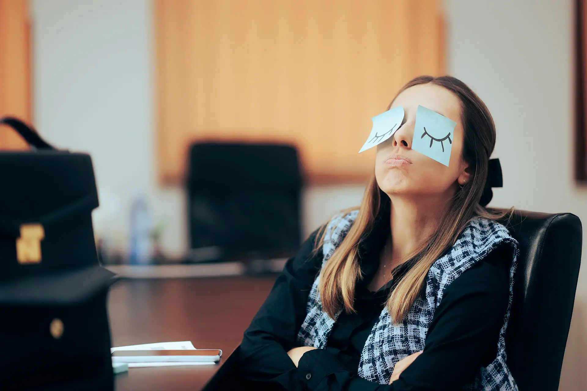 Employee Engagement image shows a lady at her desk with two sticky notes over her eyes that depict closed or sleeping eyes. Disengaged Employee concept