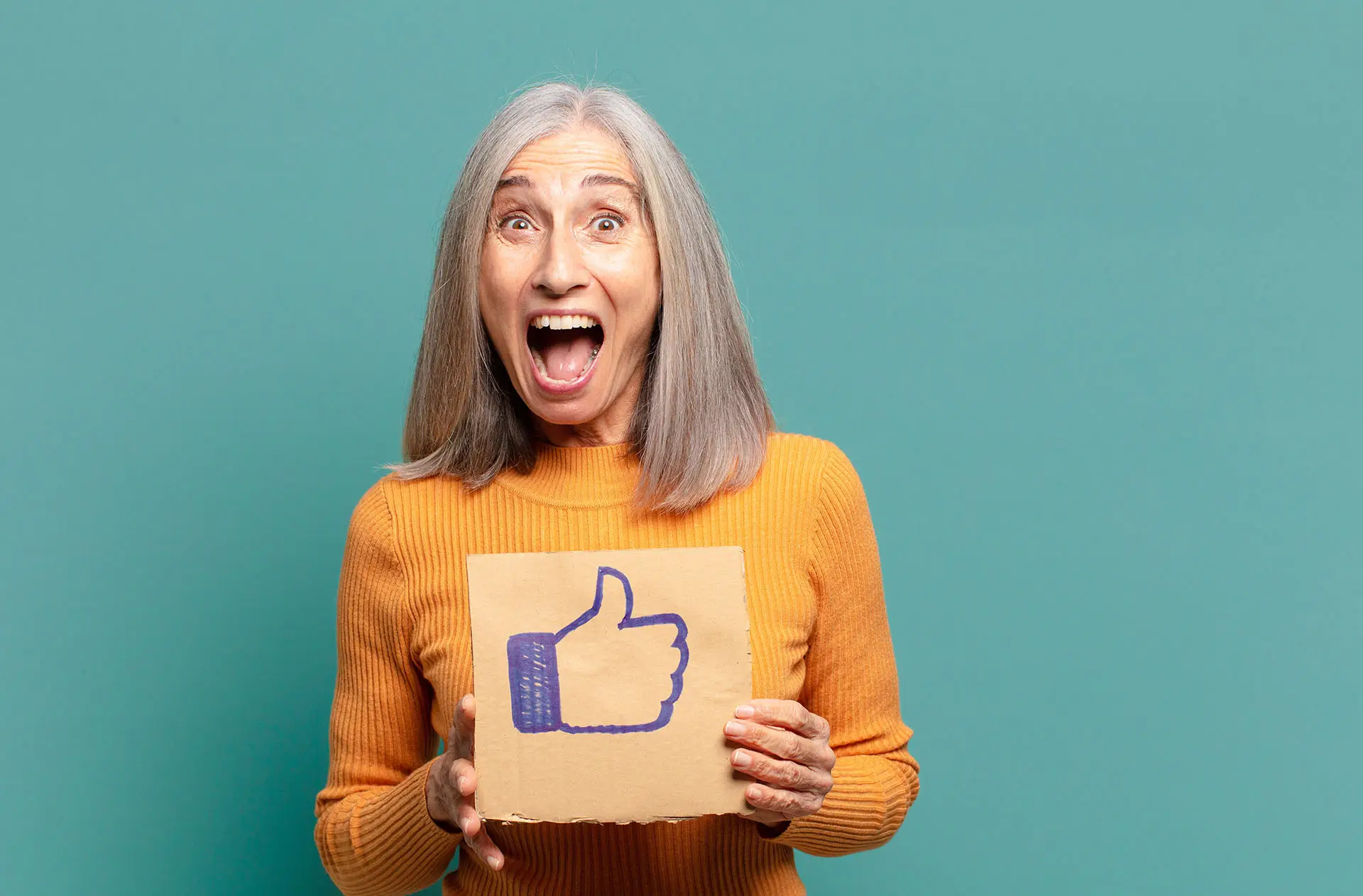 Facebook Save Feature, this image shows a happy, mature lady in a yellow jumper holding a piece of cardboard with a thumbs up on it - Facebook save feature concept