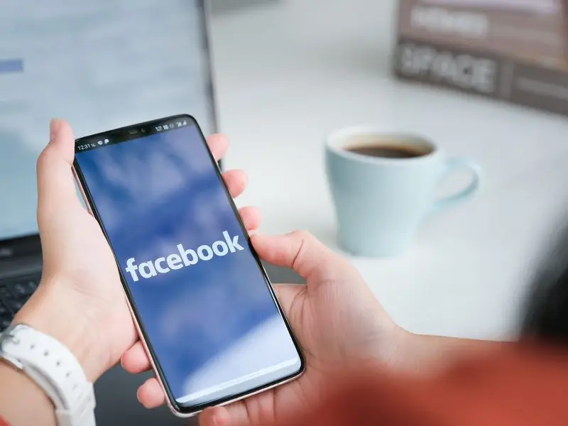 Facebook Success Story - this image shows a person sat at their desk with a phone in their hand the screen is loading Facebook