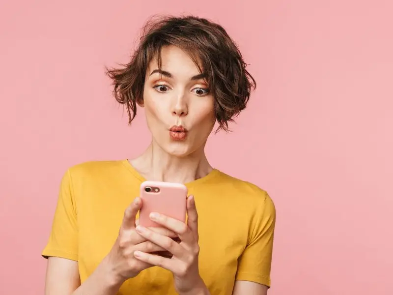 Google Update Mobile Friendly Websites this image shows a pick background with a lady in a yellow top looking at her phone with an ooh expression on her face