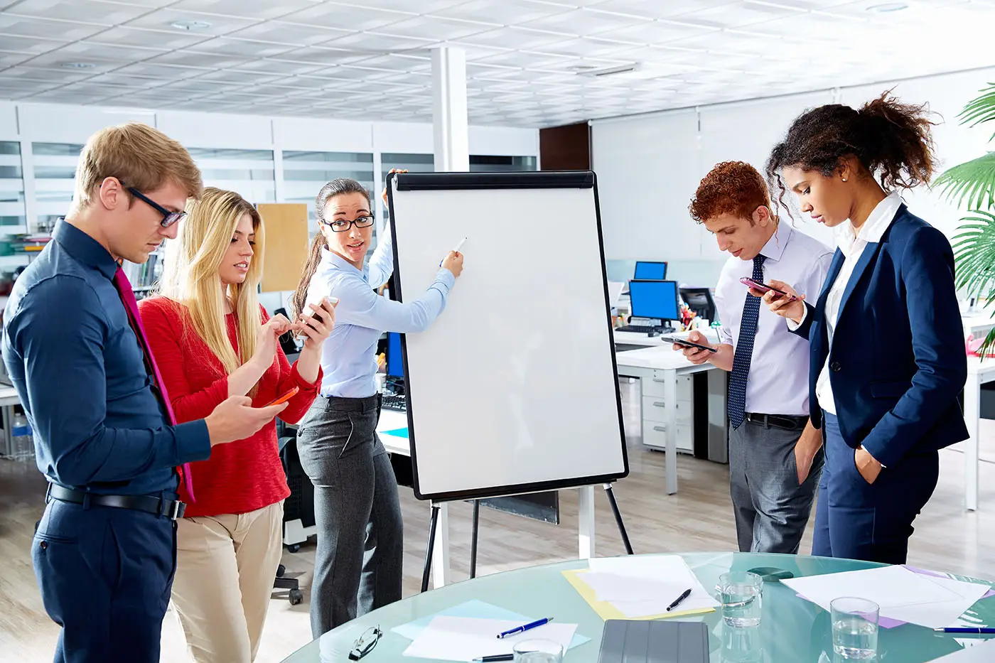 Managing Social Media Distractions images shows a team with a lady art a white board explaining a concept but all other team members are engrossed in their phone