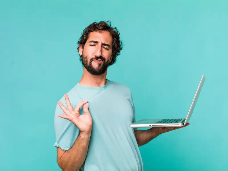 Put Some Personality into Your Blog Posts. This image is a bright blue background with an interesting looking man holding a laptop, looking opleased with himself and making a gesture that chefs would use when they have created a rather tasty dish - concept for Put Some Personality into Your Blog Posts