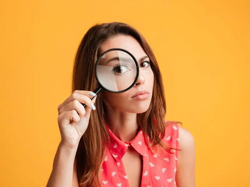 Read the Small Print - this image shows a bright yellow background with a serious woman holding a magnifying glass up to her eye