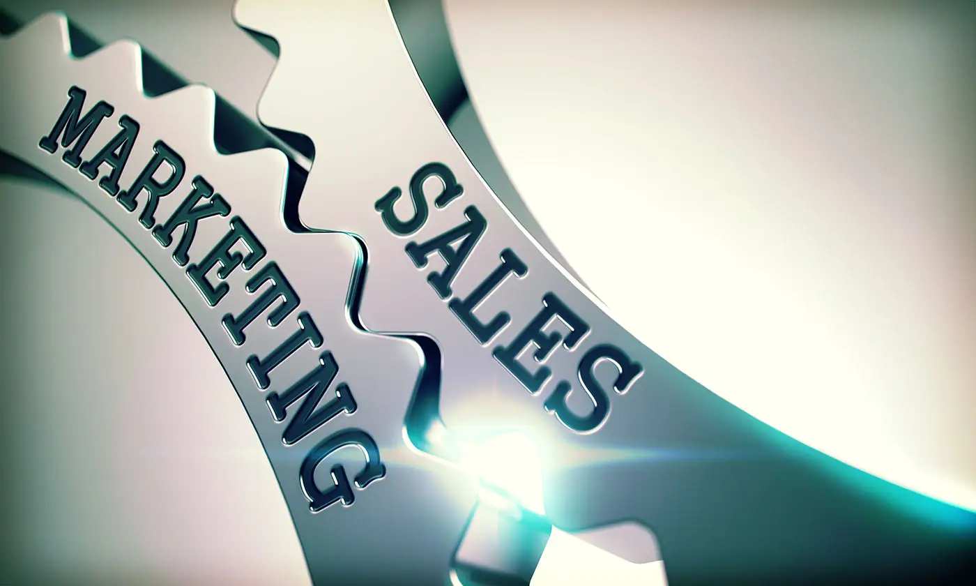 Sales and Marketing - Different Sides of the Same Coin this graphic shows two gears slotted perfectly together one has sales and the other marketing etched onto it - sales and marketing teamwork concept