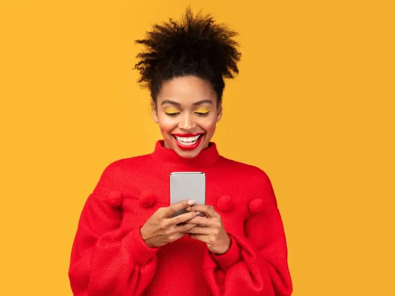 Social Media Principles - this image has a bright yellow background with an attractive lady in a bright red jumper and a large smile looking at social media on her mobile phone