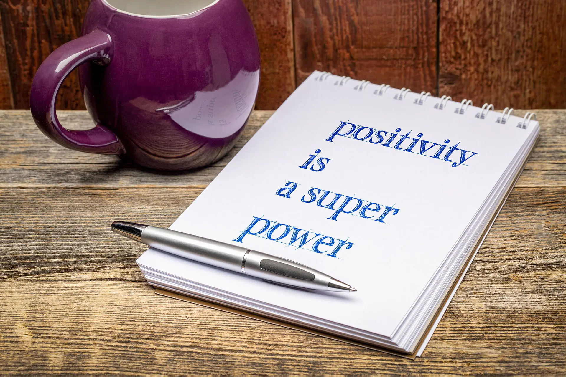 The Power of Positivity. This image shows a desk with a cuppa a pen and pad which says: positivity is a super power.