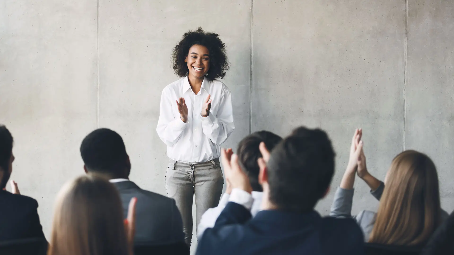 Tips for an Effective Networking Pitch. This image shows a lady stood up speaking at a business event, she is smiling and others are clapping. Concept for Tips for an Effective Networking Pitch