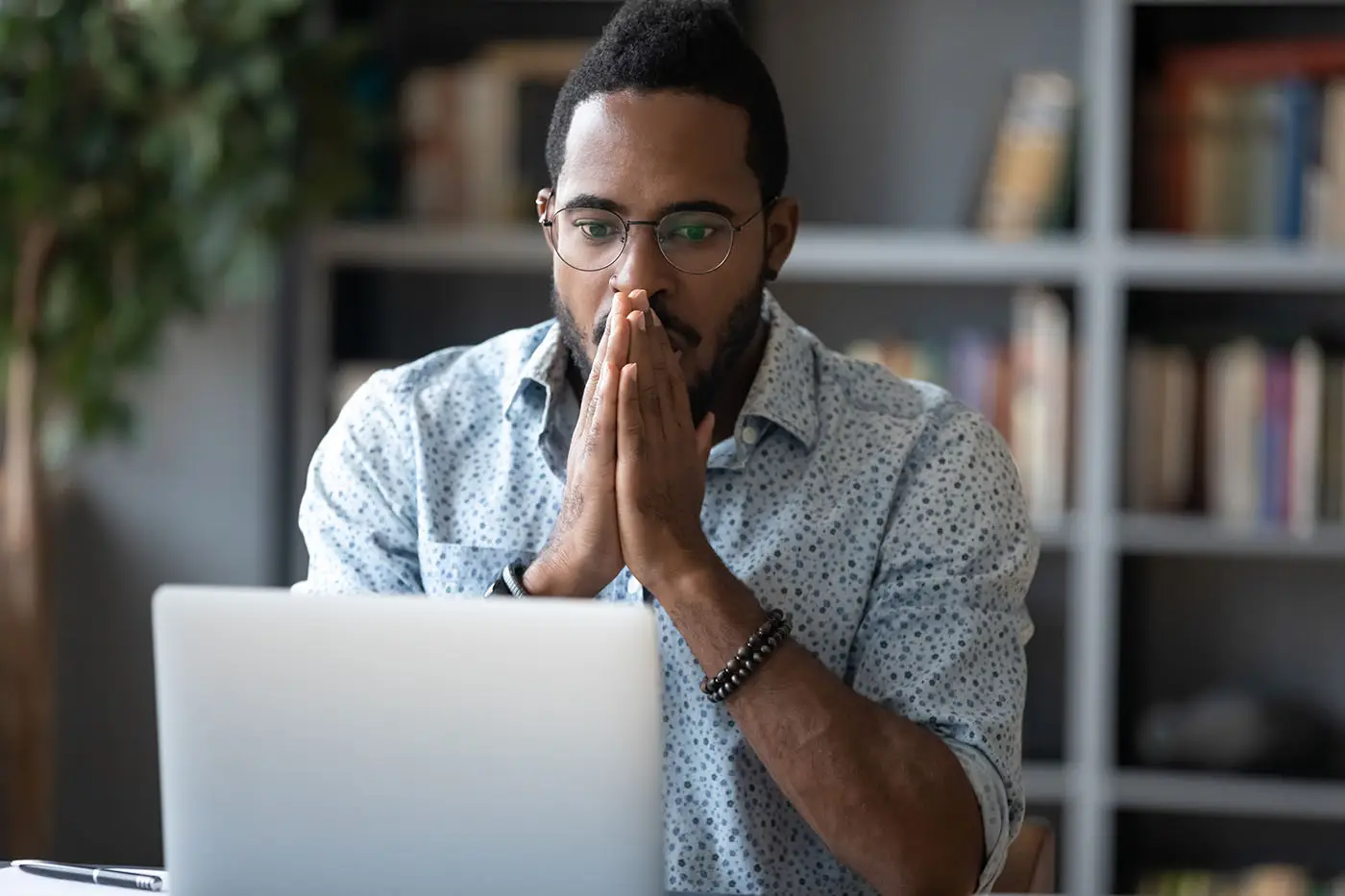 Understanding Features and Benefits this image shows a man looking at his laptop with his hands together almost like a prayer and pressed to his mouth - concept for understanding why benefits are so important