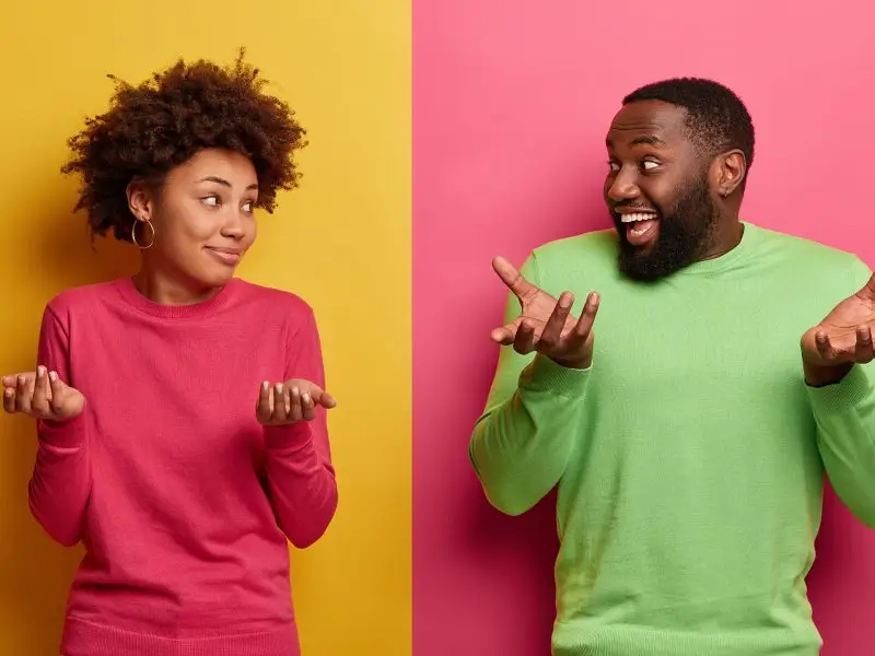 What to Blog About this image is a split screen a lady in a pink jumper with a yellow background on the left and a man in a green jumper and a pink background of the right, they are looking at each other with their arms raised in a shrug - what to write about concept