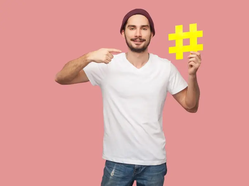 Why Hashtags Are So Important image shows a man holding up a yellow # set against a pink background