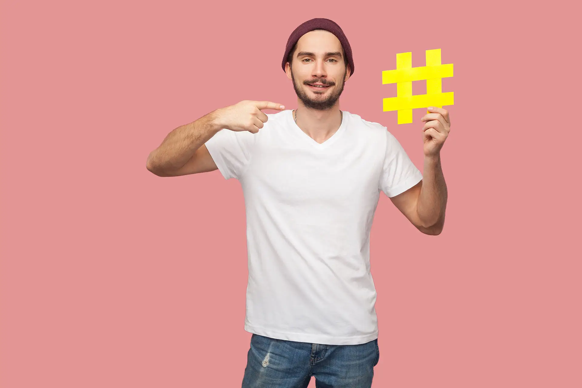 Why Hashtags Are So Important image shows a man holding up a yellow # set against a pink background