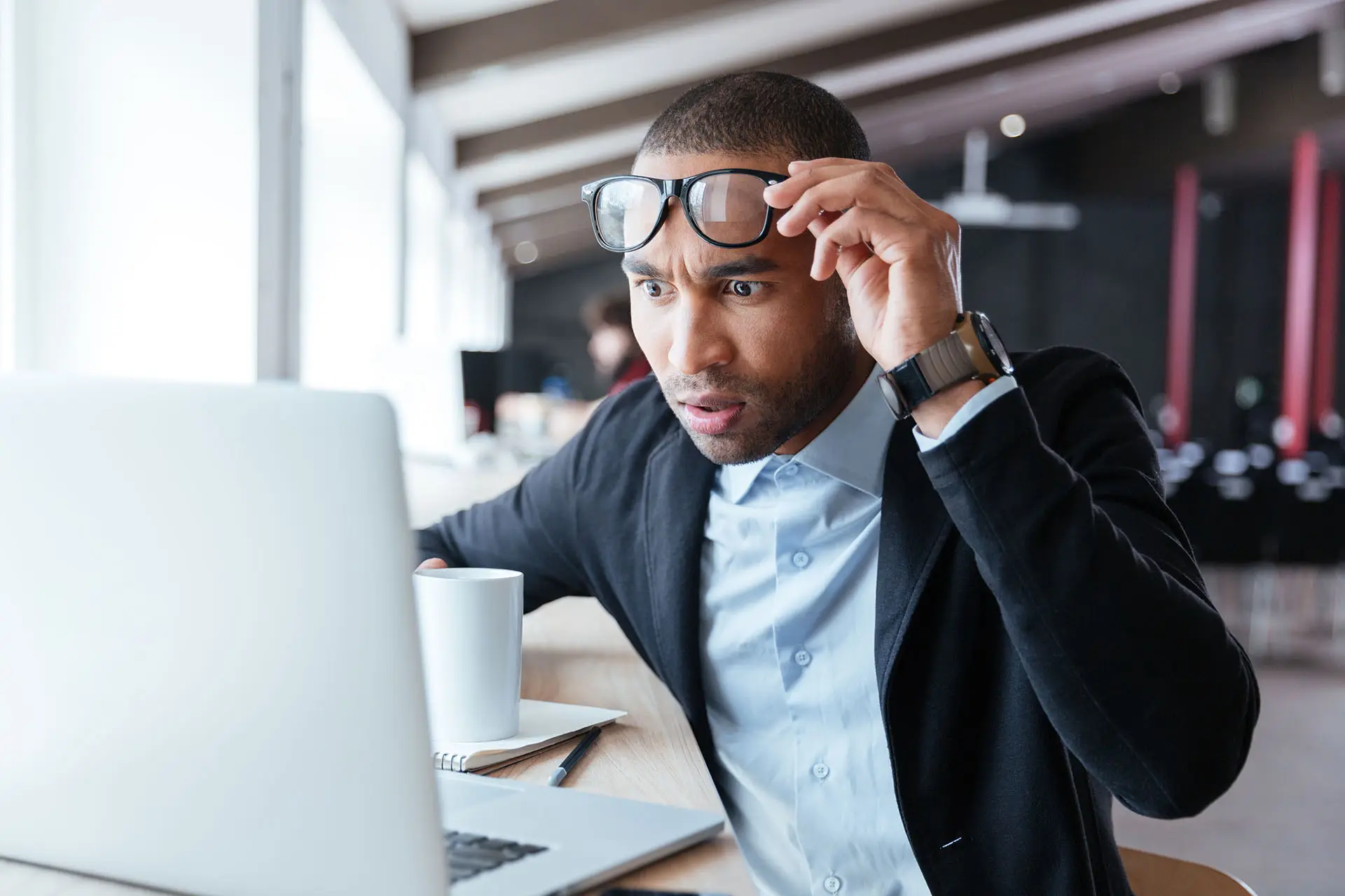 Why High Google Bounce Rates Can be Good. The image shows an attractive man looking at his laptop, he has raised his glasses and staring at the screen in disbelief