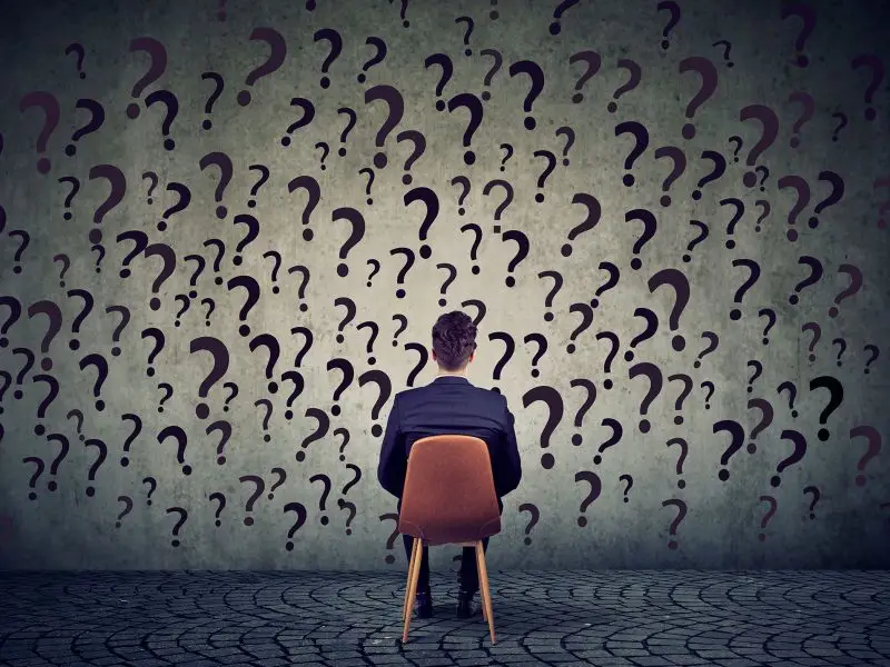 You’ve Gotta Have a Plan Stan - Image shows a man sitting on a chair facing a grey wall which is covered in question marks - business development planning concept