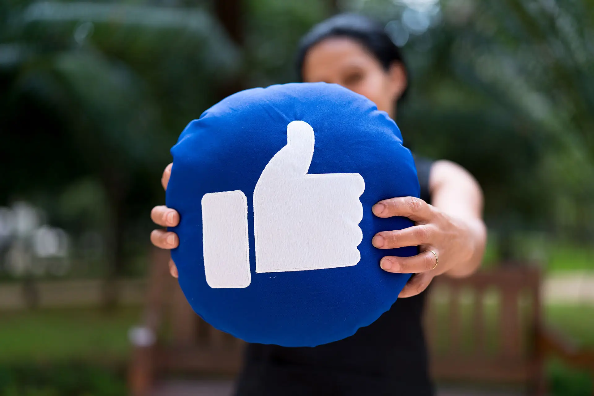 Could the New Facebook Green Badge Boost Your Business Online? This image shows a lady holding out a cushion with the Facebook Thumbs up sign