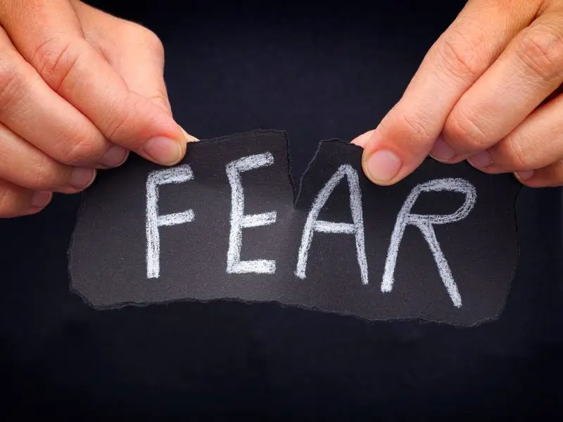 Fear Doesn't Stop Me. This image shows a picture of a person holding a piece of black paper with the word fear on it,m the person is ripping this in half