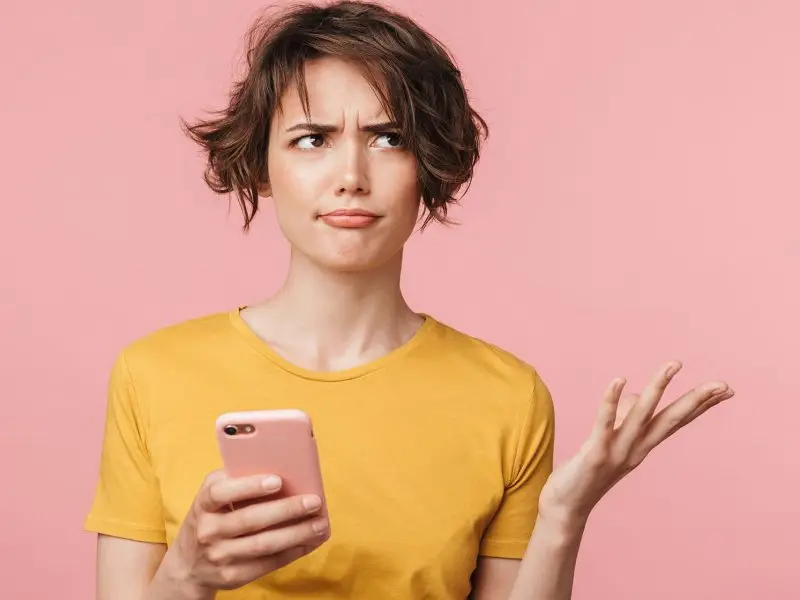 Google Algorithm Launch on 1st November - this image shows a pink background with a lady in a yellow top holding her mobile phone with her eyes rolled and her hand up questioningly