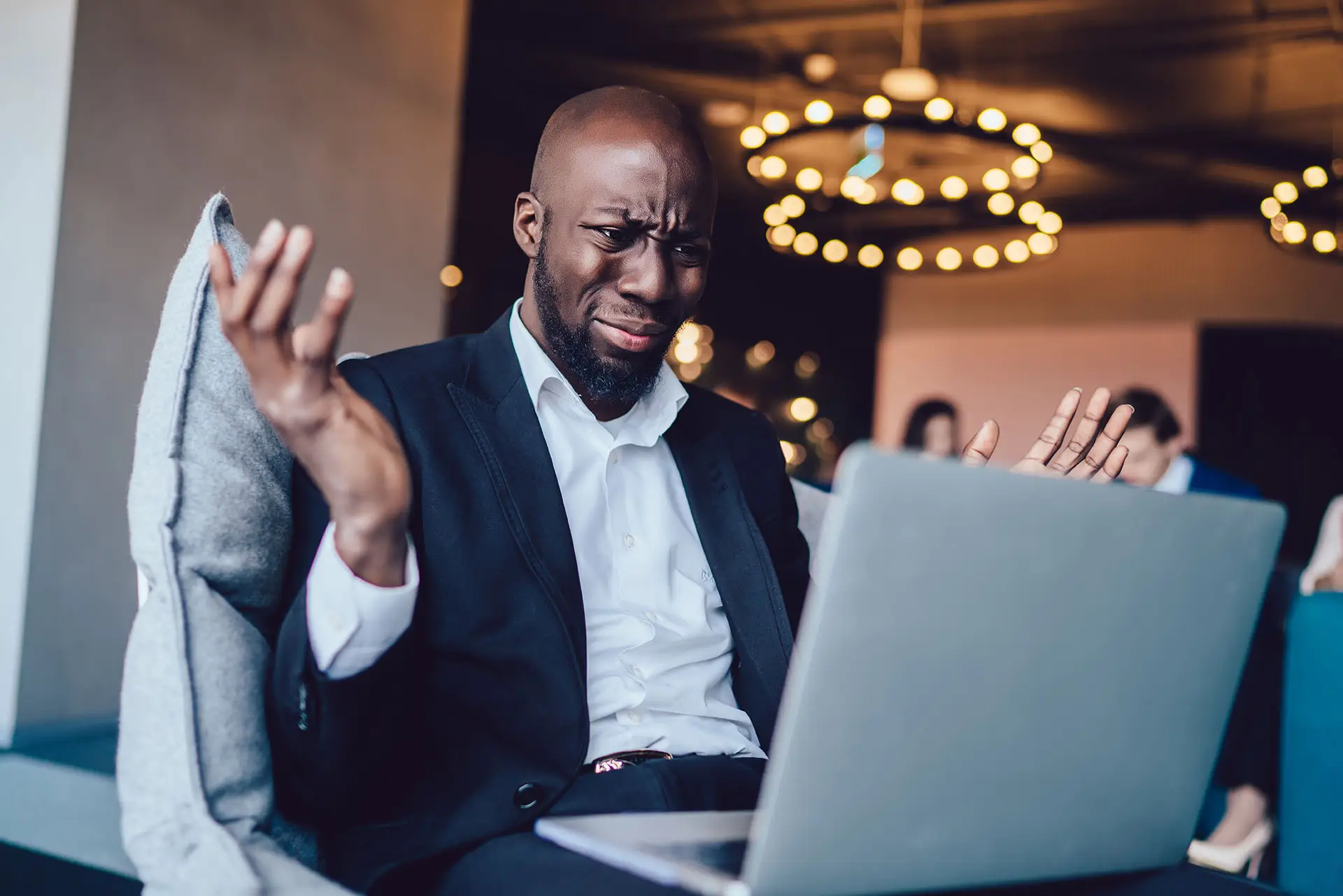 How to Change Your Facebook Business Page Name - this image shows an attractive man sitting with his laptop on his lap, both arms are raised and his face suggests he is frustrated.