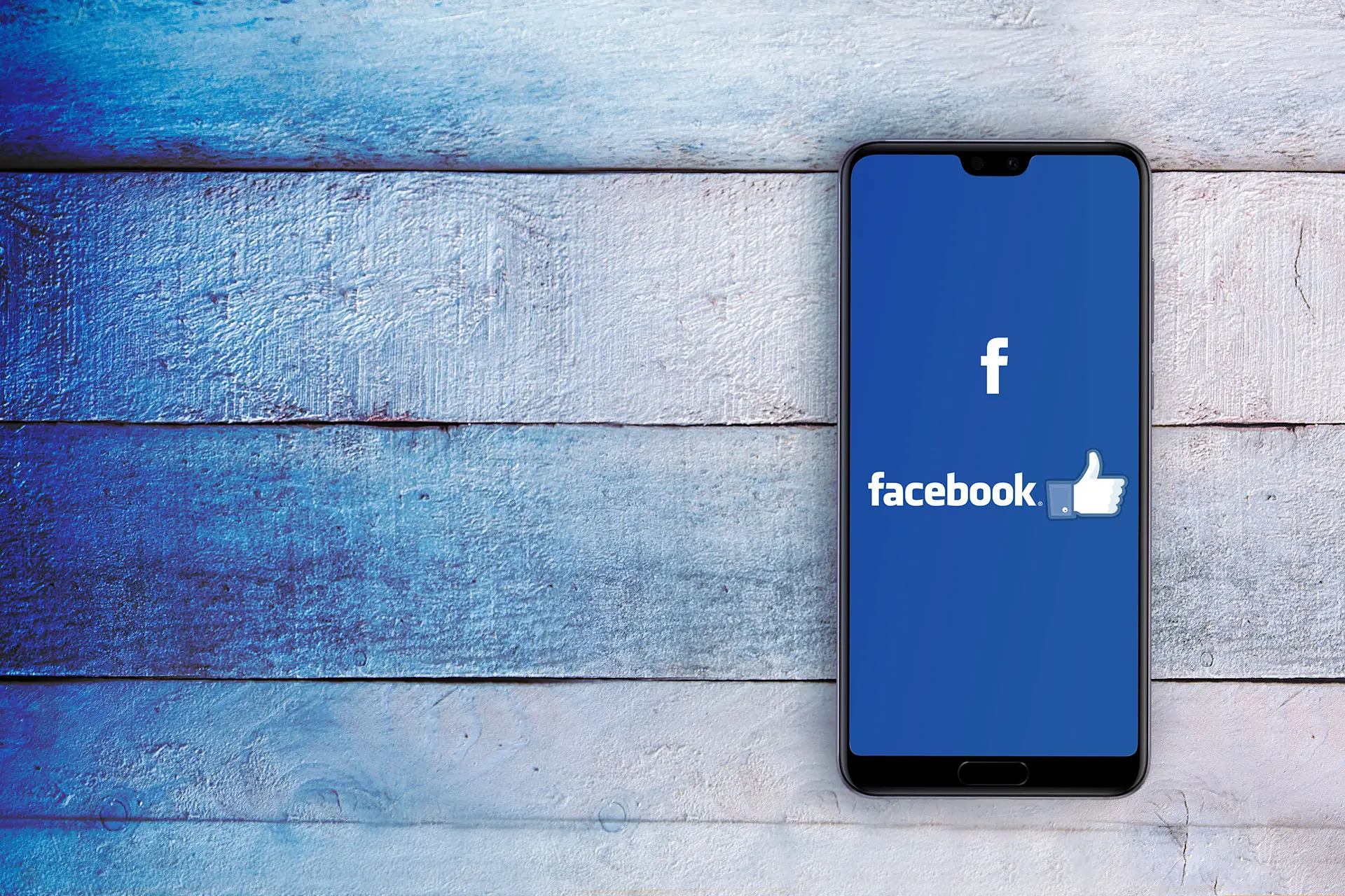 Our Facebook Success Story - this image shows a phone sitting on a rustic wooden table, the phonce screen shows the Facebook blue screen and logo