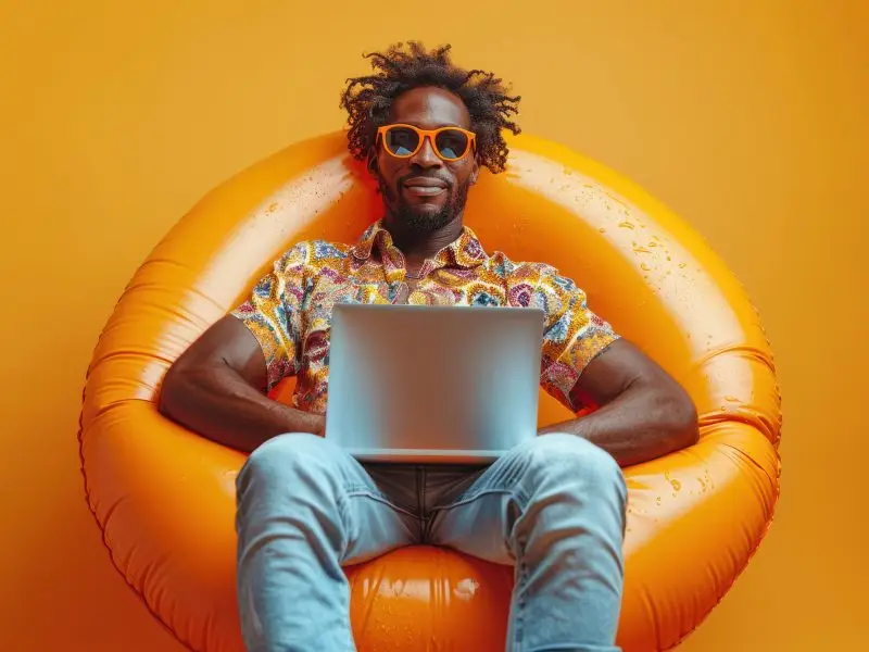 Practices to Avoid When Adding Content to Your Website this image shows a very relaxed man sitting on an inflatable chair wearing sunglasses and a bright holiday shirt, he is working on a laptop - concept for adding content to your website