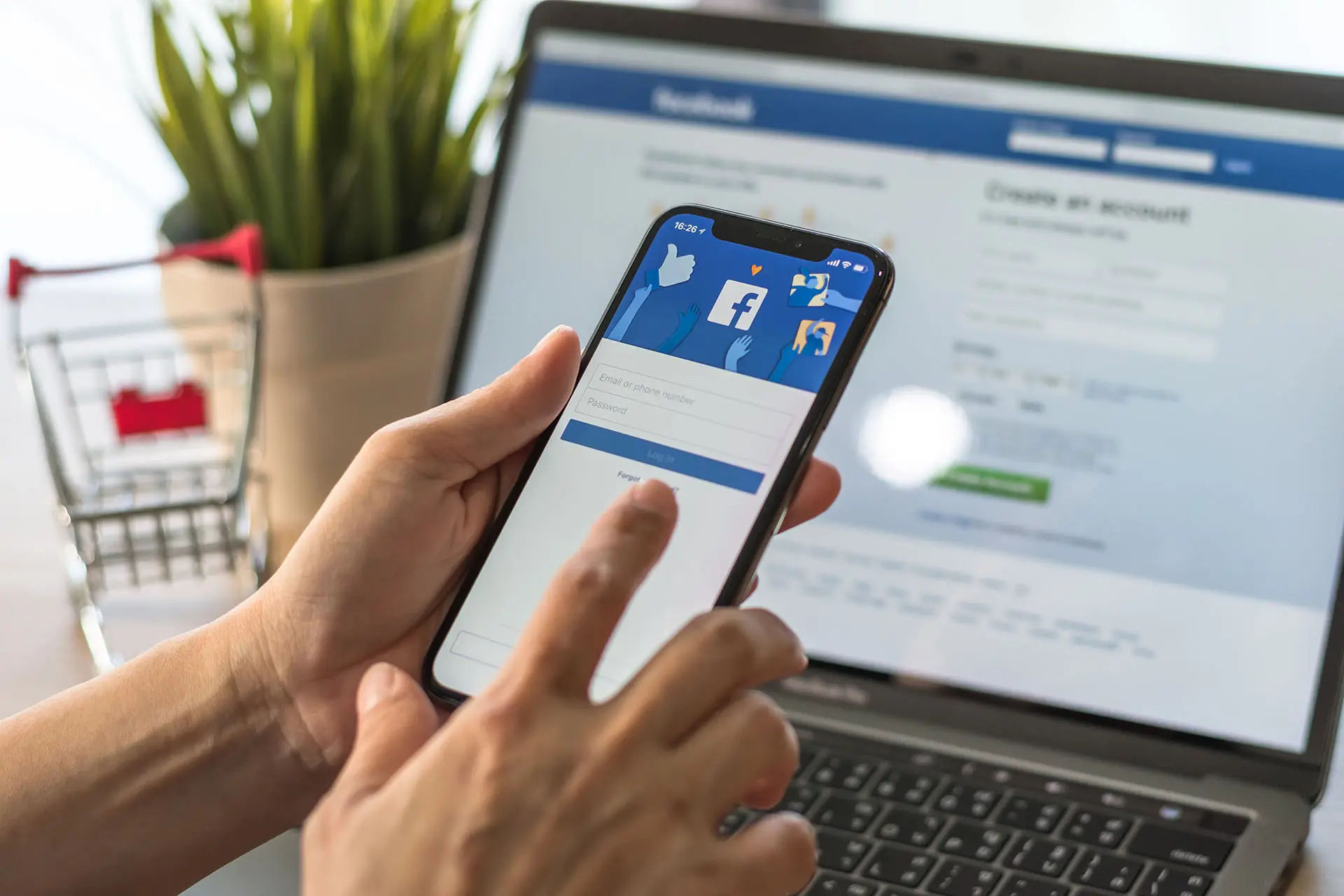 Using Facebook as Your Business Page - this image shows a user with a mobile phone logging into their Facebook Business Account, with a similar screen showing on a laptop in the background