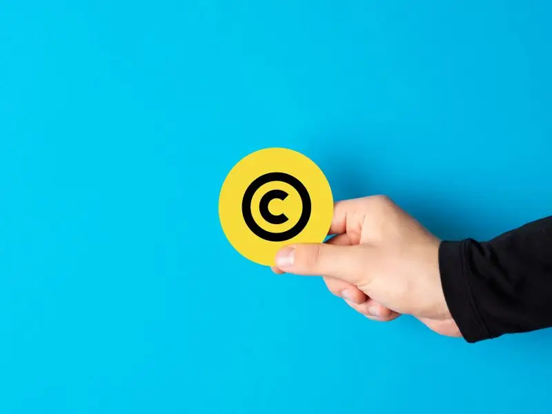 Website Content Theft - this image shows a bright blue background with a hand extended from the right holding a yellow copyright symbol - concept for Website Content Theft