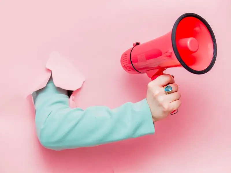 What is Remarketing? This image is of a pink paper wall with an arm reaching through holding a megaphone - concept for remarketing