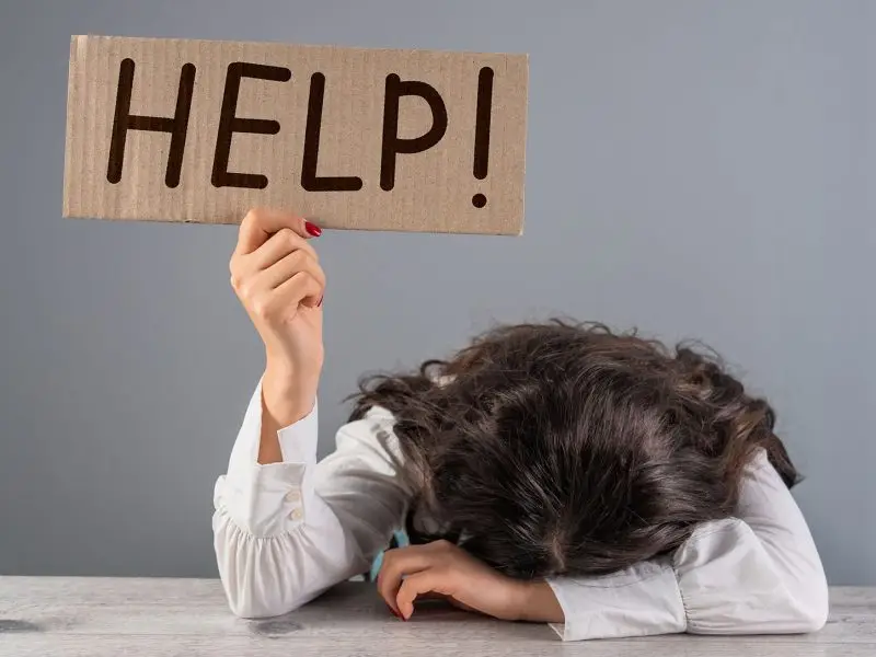 And Faith is Restored… this image shows a lady seated at a desk with her head resting on her arms/desk, she is holding up a cardboard sign that says "help!"