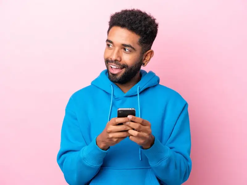 Facebook Messenger Ads this image shows a pink background with a man in a blue top smiling and looking up from the phone that is in his hands