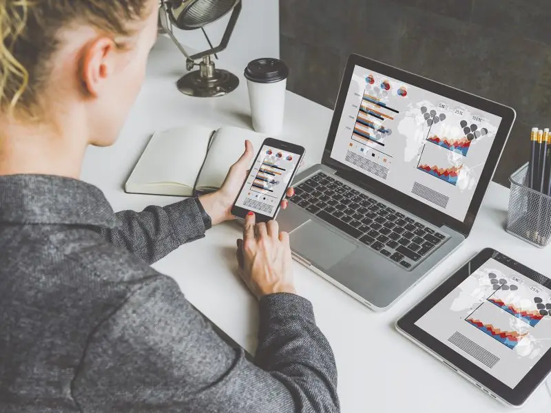 Google Assets for Small Businesses - this image shows a lady sat at a desk with a laptop, tablet and phone all showing analytical data