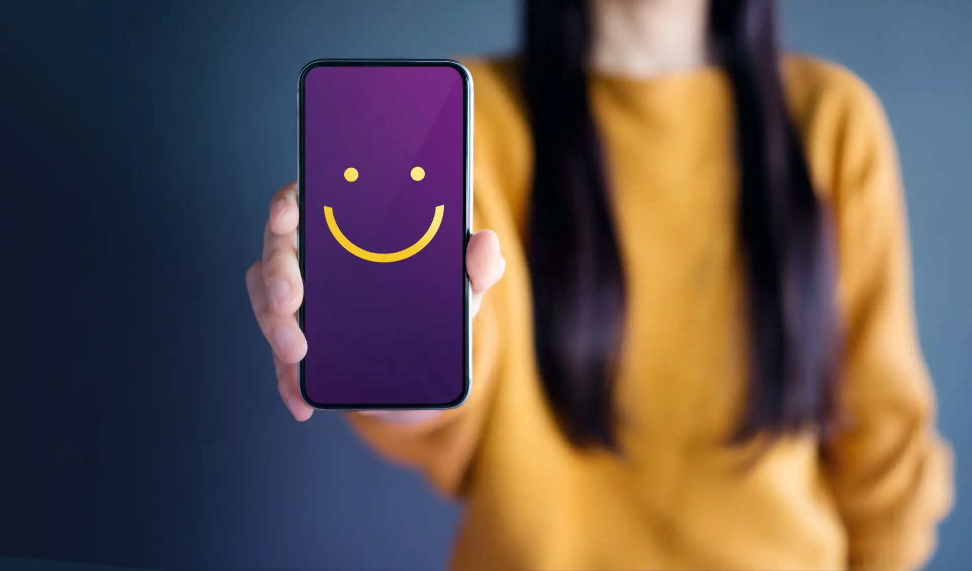 Google Core Web Vitals - this image shows a lady in a bright yellow jumper holding out a mobile phone, on the screen is a purple background with a yellow smiley face - concept for a happy, healthy website