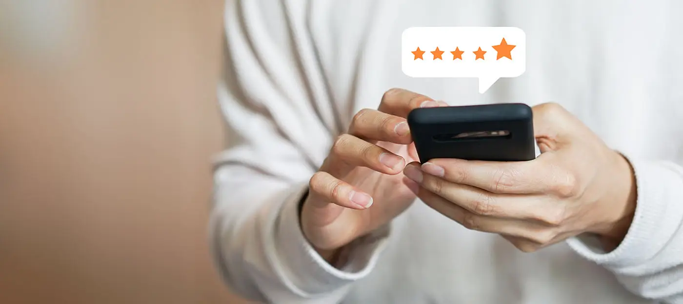 Google My Business - this image shows a user holding a mobile phone, writing a review, there is a graphic above the phone with 5 stars similar to the rating that Google uses