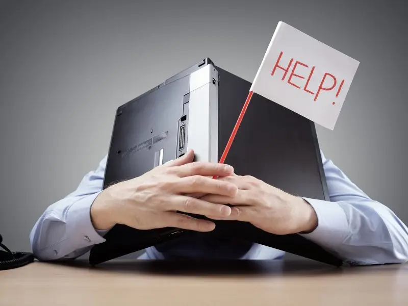 How to Overcome Bloggers Block - this image shows an man slumped on his desk with his laptop over his head, he is holding a small white flag with the word help on it. Concept for bloggers block