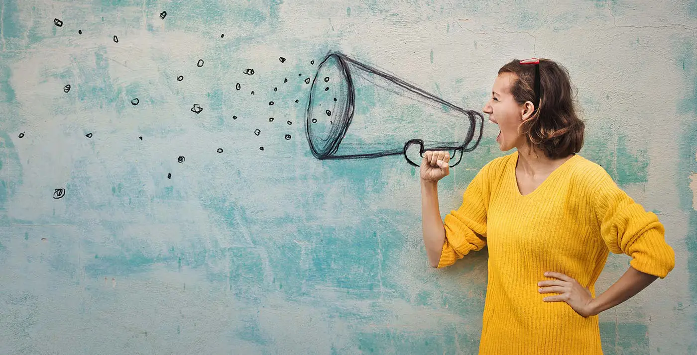 How to Write a Press Release - this image has a sky background, in the foreground is a lady in a yellow jumper, she is using a drawn megaphone