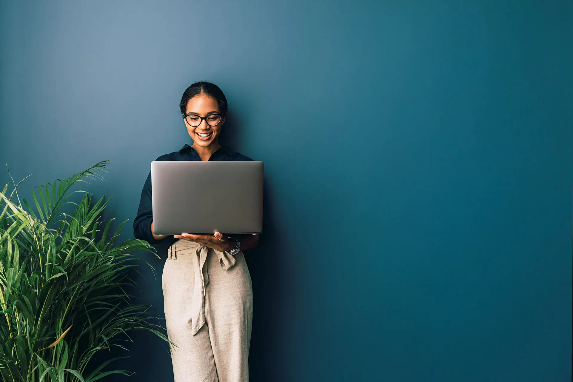 Introducing Workplace by Facebook - this image shows a lady leaning against a petrol blue wall holding her laptop and smiling