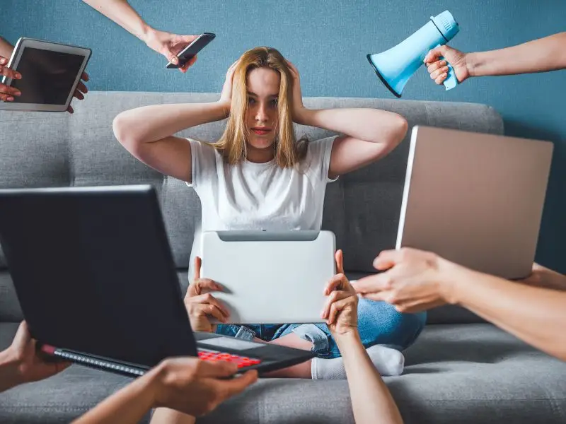 Is “Fake News” News? This image shows a young girl sat on a sofa with her hands over her ears and lots of hands holding various devices including a laptop mobile, tablets and a megaphone. Concept for a deluge of fake news