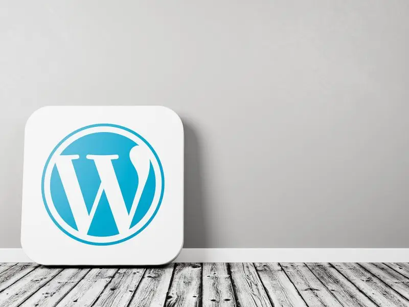 Major New WordPress Update - this image shows a grey wall and a grey wood flooring with a white tile with the WordPress "W" icon which is leaning against the wall