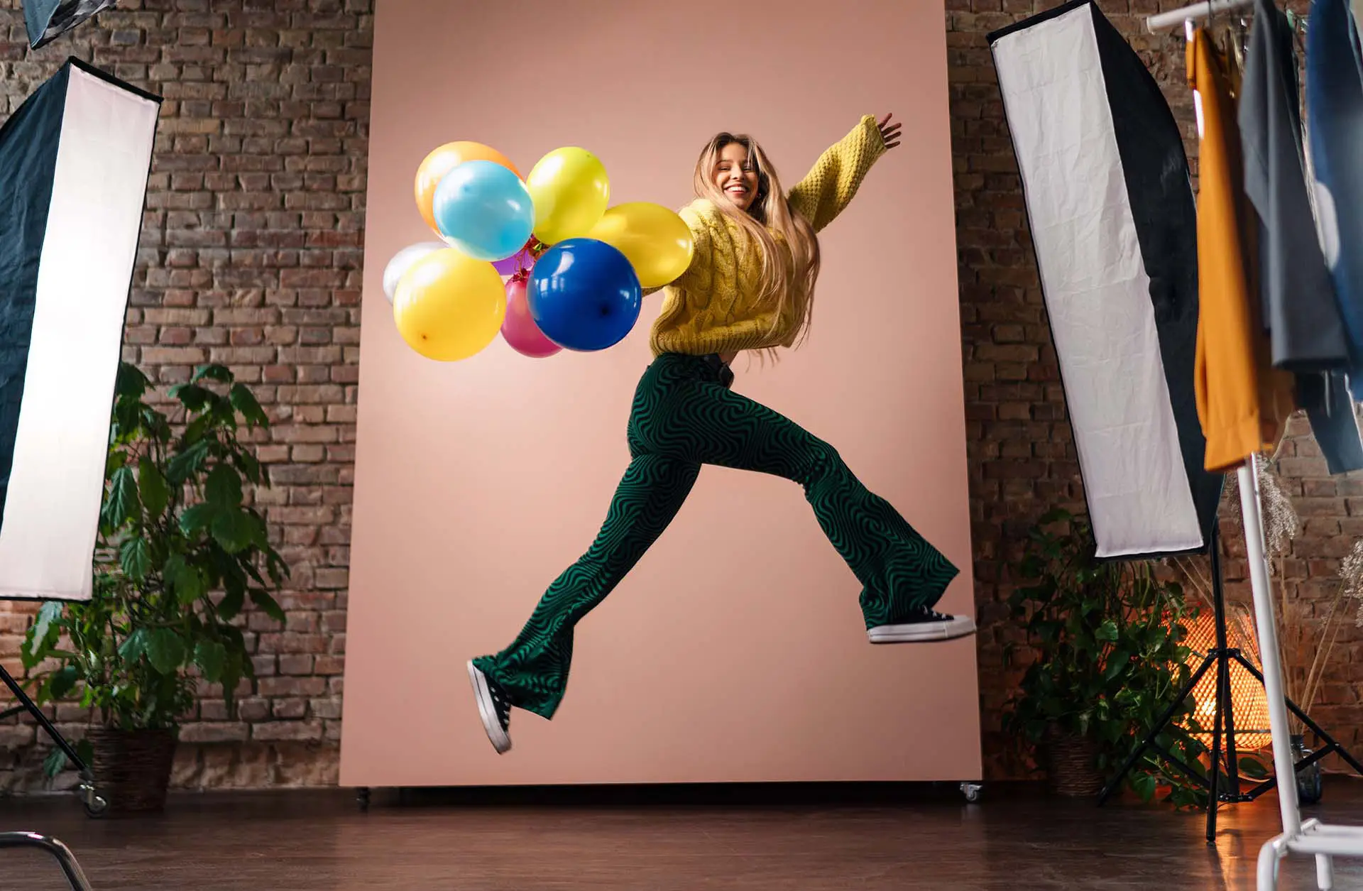 Product Photography Tips - this image shows a product photoshoot, there is a lady holding balloons, wearing a funky yellow jacket, flared green trousers and she is leaping through the air