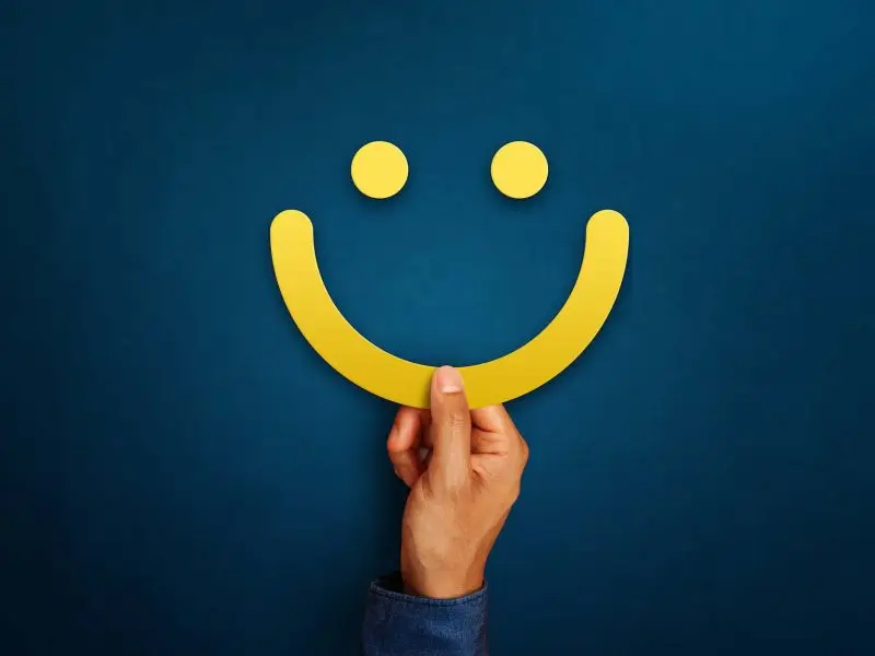 The Importance of Customer Reviews and How to Encourage Them - this image shows a dark blue backgrpound with a bright yellow smiley face in the middle of the screen, the smile is being held up by a hand