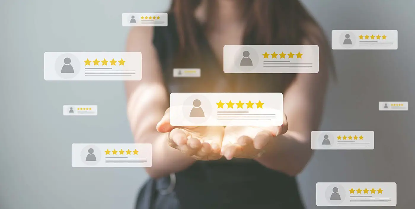 The Importance of Customer Reviews and How to Encourage Them - this image shows a light grey, slightly blurred backgrpound, with a lady holding her pals out, above her palms are various boxes all containing 5 star reviews