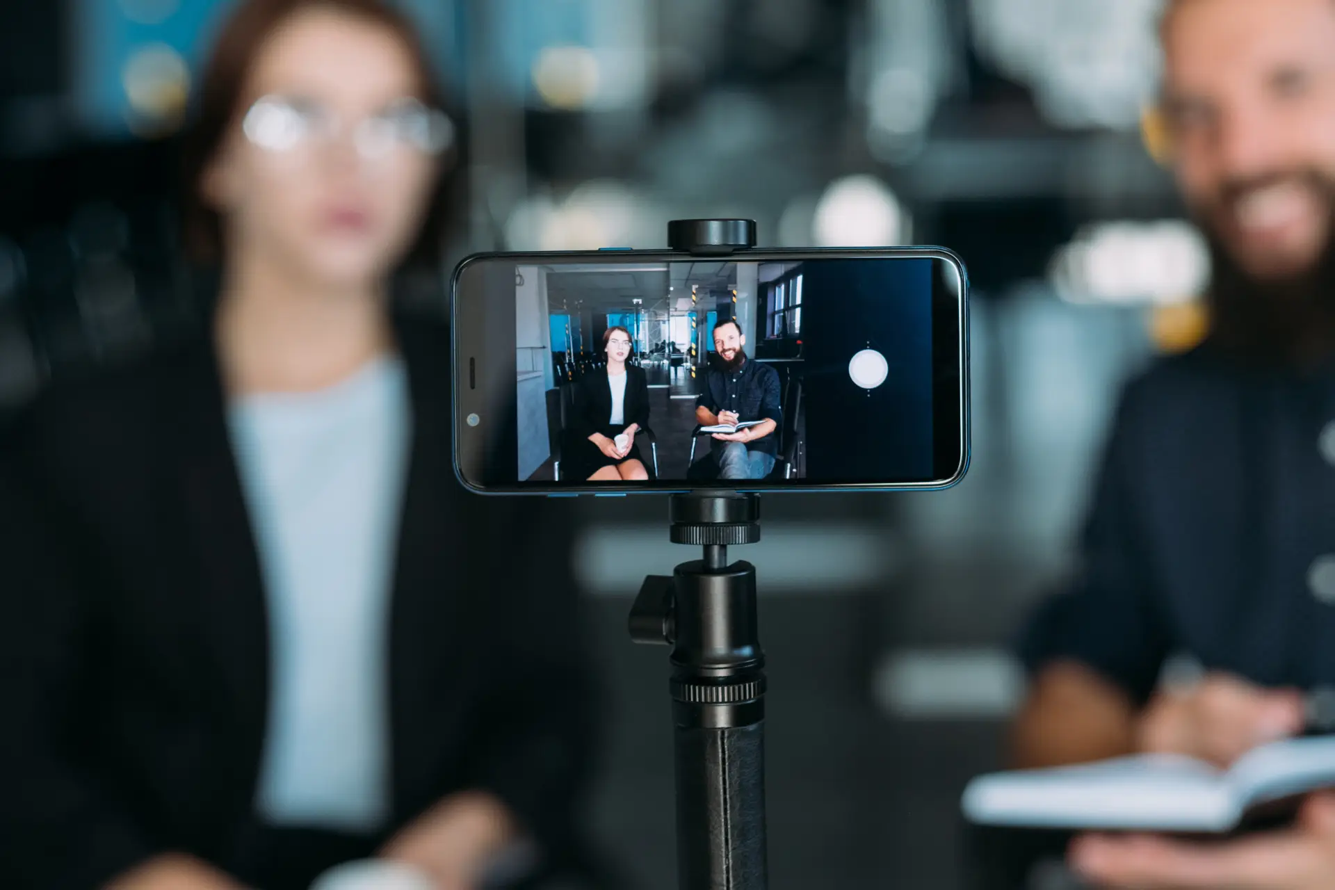 Tips for Using Video on Social Media - this image shows a man and woman in the background with a camera phone on a tripod in the foreground recording them