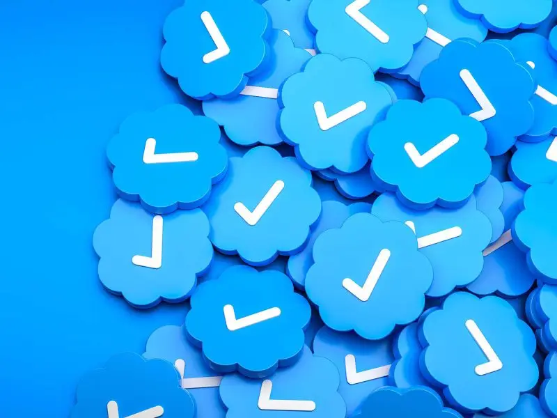 Twitter Blue Tick - this image shows a blue background with a pile of blue discs each with a tick on it - concept for twitter blue tick