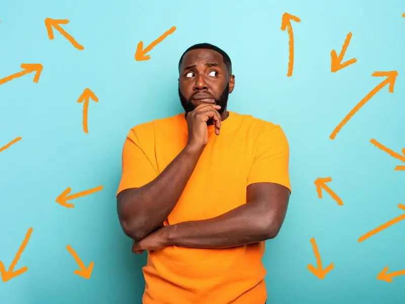 Website Redirects this image shows a light blue background with a man in an orang tshirt looking perplexed, the wall behind him has orange arrows pointing in multiple directiomns, concept for website redirects