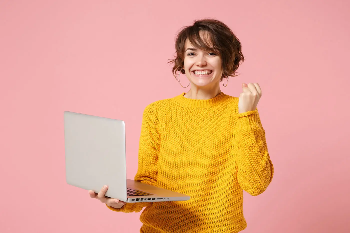 What Should be Included on a Product Page - this image shows a light pink background with a lady in a bright yellow jumper in the foreground, she is holding a laptop and looks excited