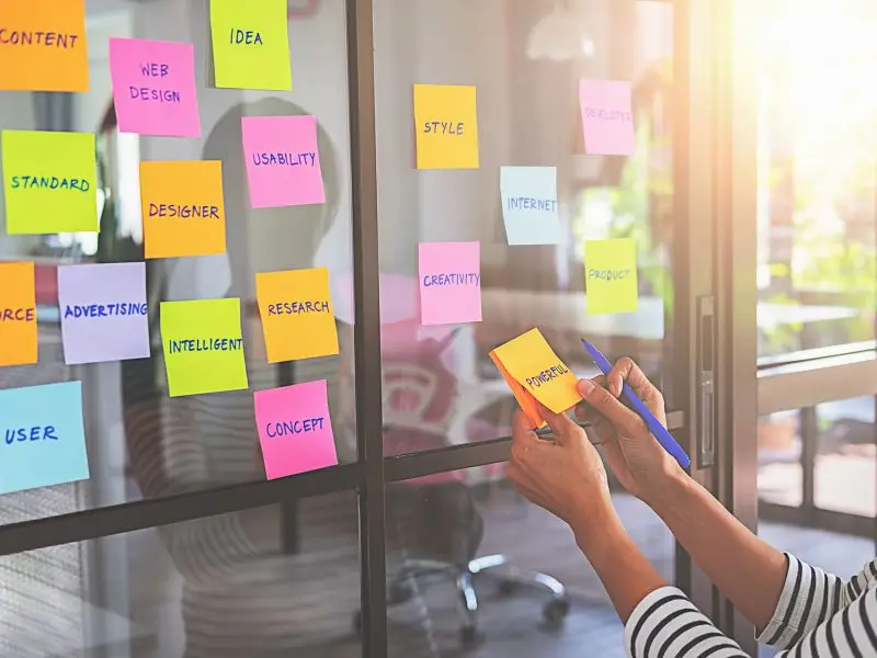 What is UX? This image shows a lady apply sticky notes to a glass wall, each has a consideration for UX - User experience